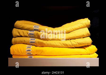 Close-up of a stack of yellow t-shirts with large and medium stickers isolated on black background Stock Photo