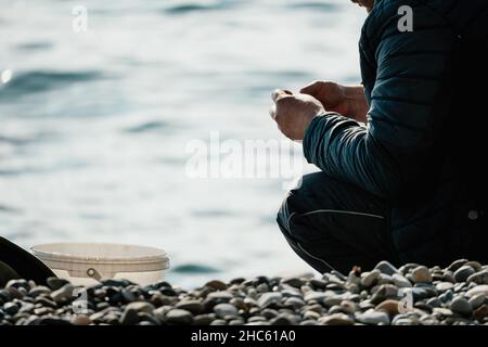 Man hobby fishing on sea tightens a fishing line reel of fish. Calm surface sea. Close-up of a fisherman hands twist reel with fishing line on a rod Stock Photo