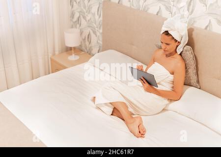 Woman wrapped in towels using her digital tablet. Stock Photo