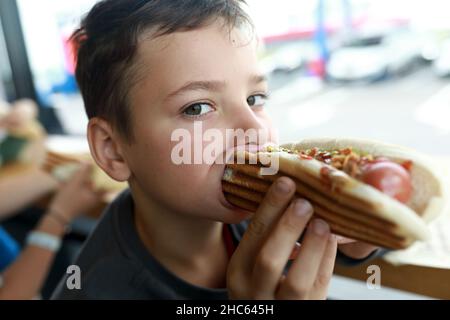 Portrait of kid eating Hot Dog in restaurant Stock Photo