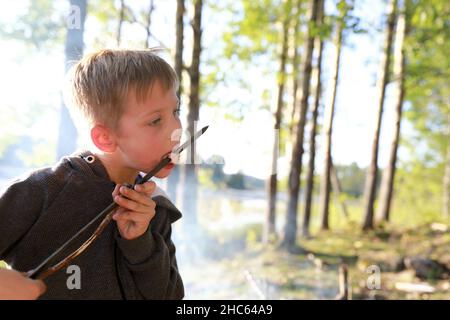 Child eating sausage on skewer in forest, Karelia Stock Photo