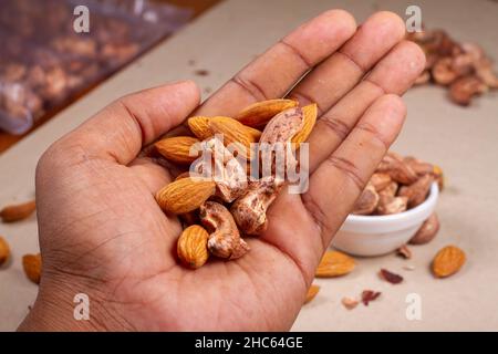 Roasted almond and cashew nuts in hand on light background isolation. Stock Photo