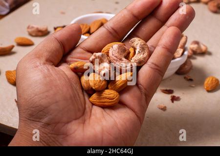 Roasted almond and cashew nuts in hand on light background isolation. Stock Photo