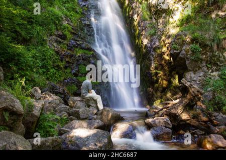 a person sits at the Todtnau waterfall in Todtnauberg in the Black Forest Stock Photo