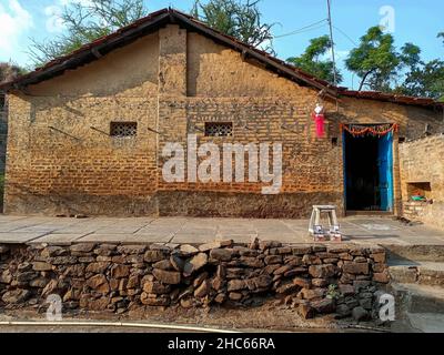 Stock photo of beautiful traditional Indian village house, red brick house with pyramid shape roof top. White color painted stool placed on the front Stock Photo