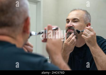 Serious handsome man looking in mirror and shaving his whiskers Stock Photo