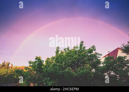 Beautiful rainbow over the village during sunset Stock Photo