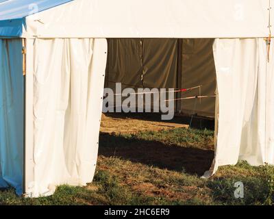 White large canvas tent lit by sun stands on the grass with ropes stretched inside Stock Photo