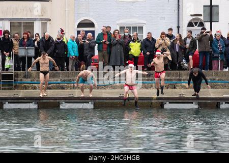 Weymouth, UK. 25th December, 2021. Contenstants jump into the water at the annual Weymouth Christmas Day Harbour Swim. Participants swim over 70m between the banks of Weymouth Harbour, raising money for the Weymouth and Portland Lions Club. Credit: Liam Asman/Alamy Live News Stock Photo