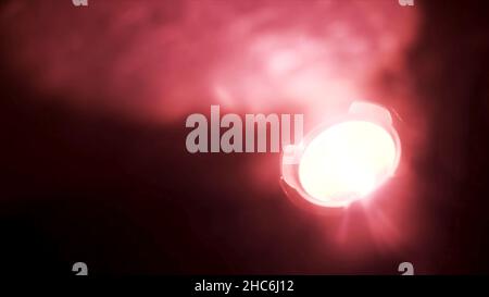 Close up of red spotlight blinking in complete darkness. Red soffit shimmering in the dark room, being turned on isolated on black background. Stock Photo