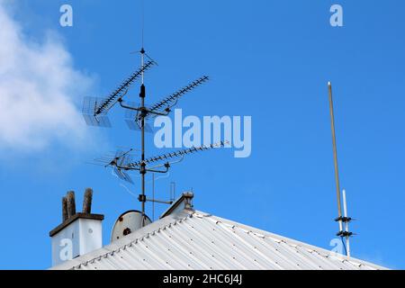Four large TV antennas put over satellite dish mounted on single strong metal pole on top of office building new metal roof next to old industrial Stock Photo