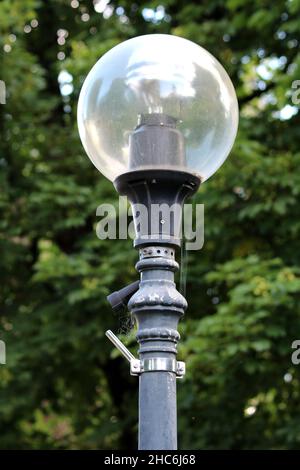 Old dilapidated vintage retro looking public street light with round glass on top and modern LED light inside and open connector left for outdoor Stock Photo