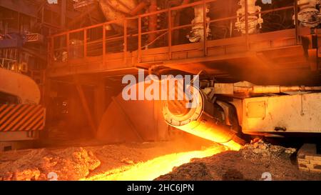 Side view of melting steel furnace big moving element in the hot foundry, metallurgy concept. Hot steel flowing in the chute at the metal melting fact Stock Photo