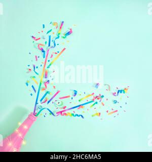 Party creative colorful confetti explosion from pink neon bottle. Flat lay, pastel blue background with copy space. Stock Photo