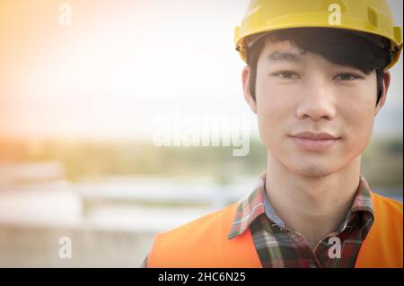 Front view of a young Asian engineer wearing reflective Orange clothing looks serious and happy. He standing on the construction project.And copy spac Stock Photo