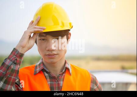 Front view of a young Asian engineer wearing reflective Orange clothing looks serious and happy. He standing on the construction project.And copy spac Stock Photo