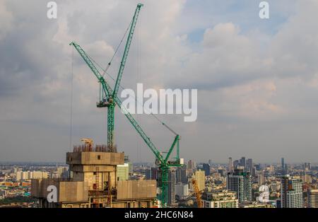 Construction cranes on a roof of a high-rise building against a cloudy sky Stock Photo
