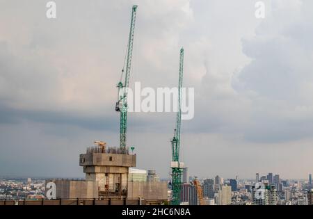 Construction cranes on a roof of a high-rise building against a cloudy sky Stock Photo