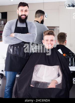 positive guy stylist demonstrating final haircut to client at hairdressing salon Stock Photo