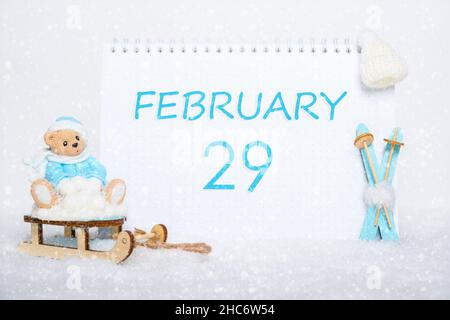 February 29th. Teddy bear sitting on a sled, blue skis and a calendar date on white snow. Day 29 of month. Winter sports concept. Winter month, day of Stock Photo