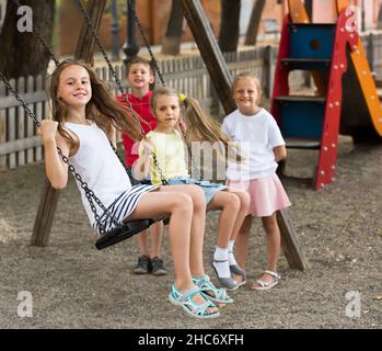 Laughing girls and boys swinging on playground Stock Photo