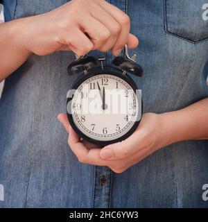 A woman holding an alarm clock that is showing a few minutes before twelve in her hands. Few minutes before deadline.. Close up. Stock Photo