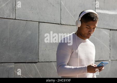 man enjoying listening to music through headphones with his phone, horizontal view with sunlight Stock Photo
