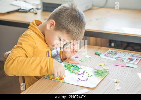 Little boy being creative making homemade do it yourself  dinosaur mosaic. Supporting creativity, learning by doing, learning through experience. Help Stock Photo