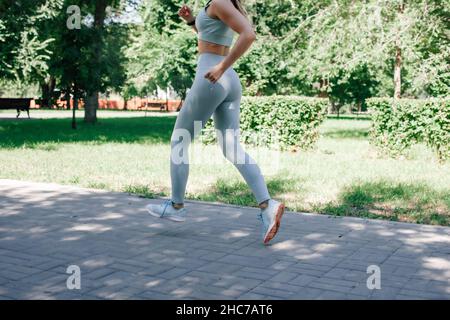 running young sporty woman warming up, stretching in grey sportswear in park in sunny summer day Stock Photo