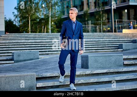 Young businessman stands on stairs near business center in suit. Stock Photo