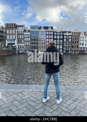 Vertical closeup of a guy standing next to the lake in front of futuristic buildings in Amsterdam Stock Photo