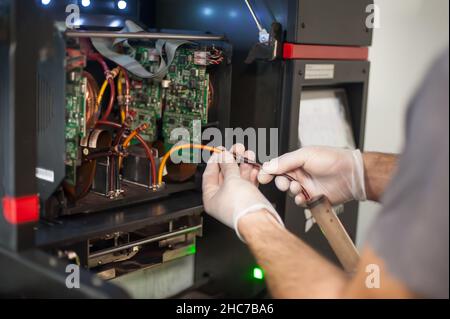 Closeup detail view of electrical engineer operator repairs large premium industrial printer and plotter machine in digital printshop office Stock Photo