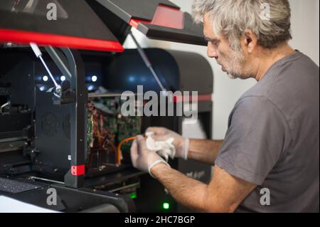 Closeup detail view of electrical engineer operator repairs large premium industrial printer and plotter machine in digital printshop office Stock Photo