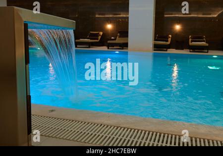 View of a beautiful interior with indoor thermal swimming pool with waterfall in a luxury lounge area of a wellness spa center Stock Photo