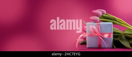 Romantic gift box tied with big pink bow and spring tulips on pink color background. Mother's day or Easter holiday concept. Stock Photo