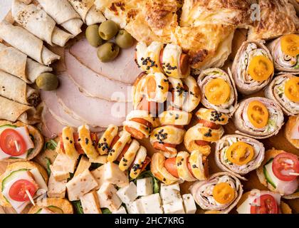 Close up on cheese and ham rolls on the wooden board plate with various food ready to eat - appetizer on the table full frame Stock Photo