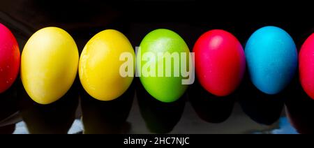 Bright, multi-colored eggs lie in a row on a rectangular black ceramic dish. Easter. Minimalism. Stock Photo