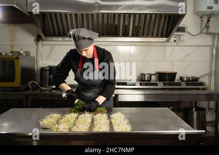 Disposable food items are ready for delivery. At the restaurant, the chef prepares food and prepares it in disposable lunch boxes. woman cuts parsley Stock Photo