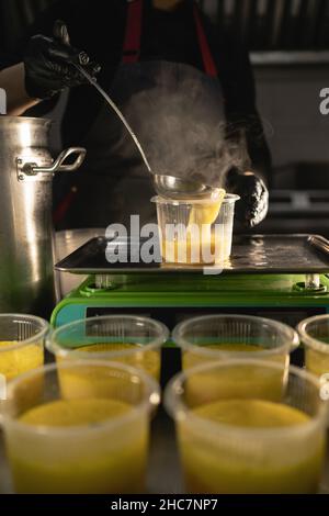 Food delivery in the restaurant. The chef prepares food in the restaurant and prepares it in disposable dishes on the scales, weighing the required Stock Photo