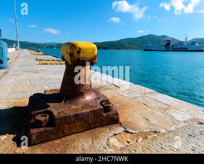 Old mooring bollard with a yellow top and rusty base in the same line with mooring chains Stock Photo