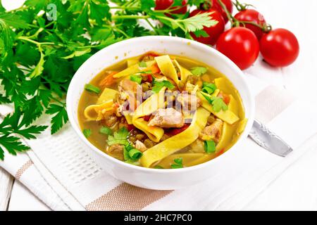 Soup with meat, tomatoes, vegetables, mung bean lentils and noodles in a bowl on napkin, parsley and a spoon on wooden board background Stock Photo