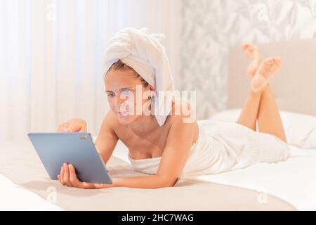 An adult woman wrapped in towels using her digital tablet. Stock Photo