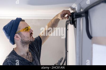 An electrician is mounting electric sockets on the white wall indoors. Stock Photo