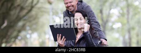 Woman in wheelchair and man talking on digital tablet in park Stock Photo