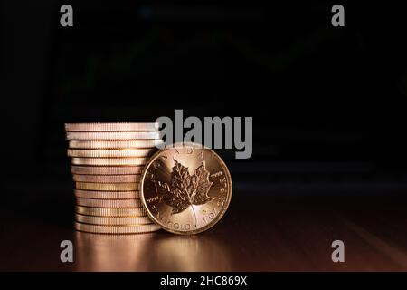 Maple leaf gold coin stands in front of a stack of gold coins Stock Photo