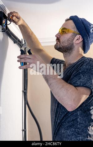 An electrician is mounting electric sockets on the white wall indoors. Stock Photo