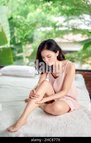 Young woman suffering from pain in leg at home Stock Photo