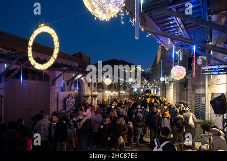 Jerusalem, Israel. 25th Dec, 2021. People walk along a Christmas decorated Bab el Gadid street in the Christian Quarter of the Old City on December 25, 2021 in Jerusalem, Israel. Israelis restricted from traveling abroad, due to the COVID-19 Omicron variant surge, filled the Christmas themed alleys of the Christian Quarter. Credit: Eddie Gerald/Alamy Live News Stock Photo