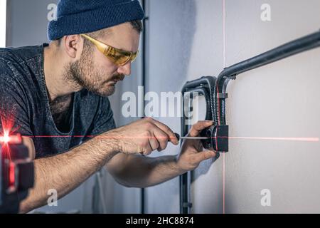 An electrician is mounting electric sockets on the white wall indoors. Stock Photo