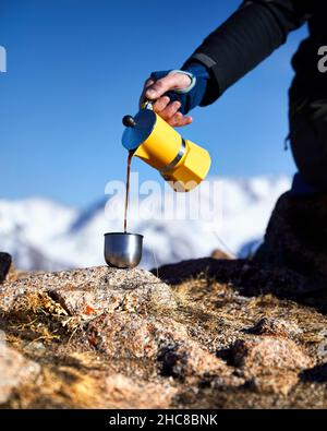 Man hiker pouring coffee from Yellow Moka mocha pot outdoors in the snow winter mountains. Old style coffee vintage pot outdoor camping Stock Photo